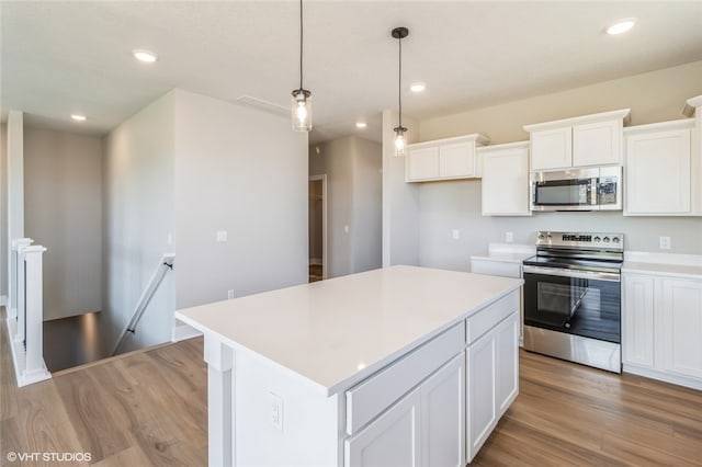 kitchen featuring light wood-type flooring, appliances with stainless steel finishes, decorative light fixtures, a kitchen island, and white cabinetry