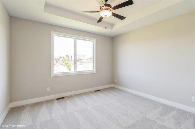 empty room featuring light colored carpet, a raised ceiling, and ceiling fan