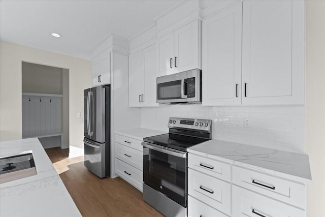 kitchen featuring appliances with stainless steel finishes, white cabinetry, light stone counters, dark hardwood / wood-style flooring, and decorative backsplash