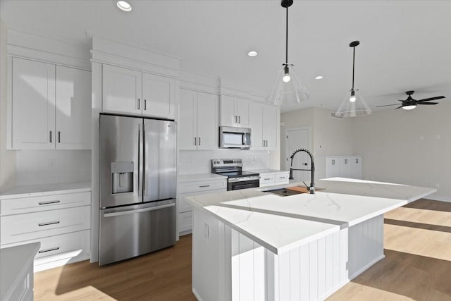 kitchen with light stone counters, white cabinetry, a center island with sink, dark hardwood / wood-style flooring, and stainless steel appliances