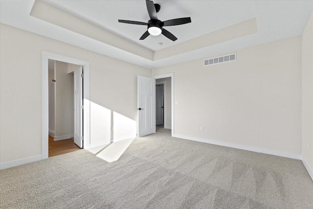 unfurnished bedroom with light colored carpet, a raised ceiling, and ceiling fan