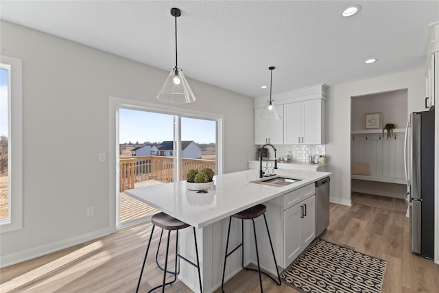 kitchen featuring stainless steel appliances, an island with sink, decorative backsplash, and white cabinets