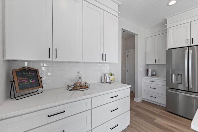 kitchen featuring white cabinetry, light stone counters, light hardwood / wood-style flooring, stainless steel fridge, and decorative backsplash