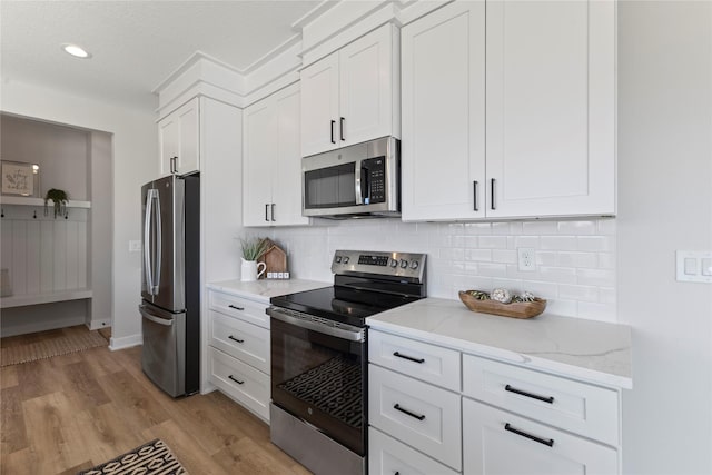 kitchen featuring white cabinetry, stainless steel appliances, light stone countertops, decorative backsplash, and light wood-type flooring