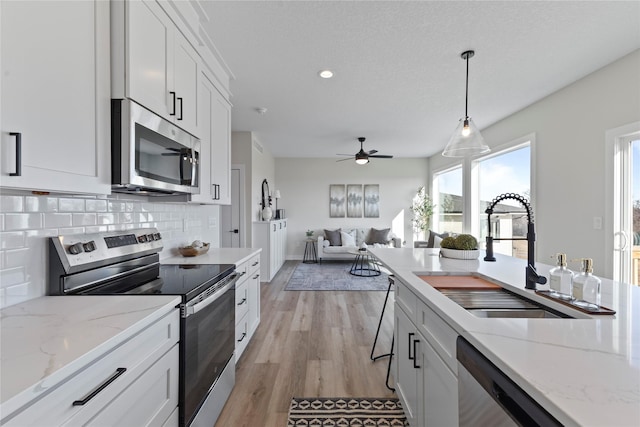 kitchen featuring sink, appliances with stainless steel finishes, decorative backsplash, white cabinets, and decorative light fixtures