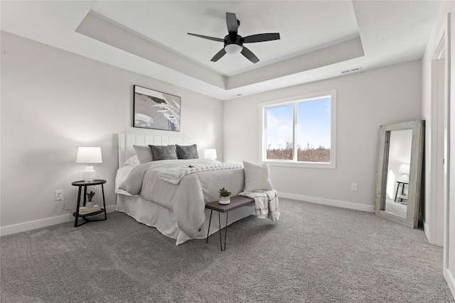 bedroom with a raised ceiling, ceiling fan, and carpet flooring