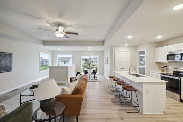 kitchen with ceiling fan, sink, a kitchen island with sink, appliances with stainless steel finishes, and light wood-type flooring