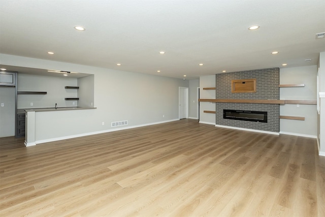 unfurnished living room featuring a brick fireplace, light hardwood / wood-style flooring, and sink