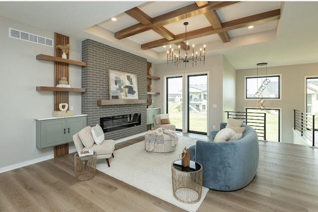 living room featuring coffered ceiling, an inviting chandelier, light wood-type flooring, beamed ceiling, and a fireplace