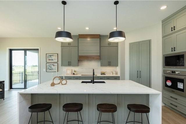 kitchen with hanging light fixtures, black microwave, stainless steel oven, light stone counters, and a large island with sink