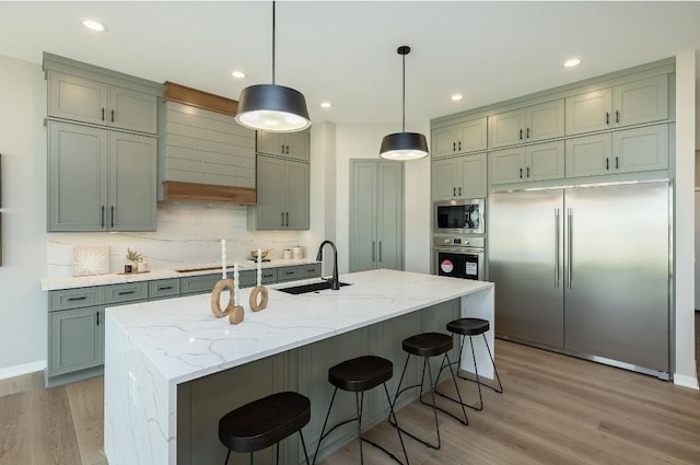 kitchen featuring an island with sink, sink, built in appliances, and light stone counters