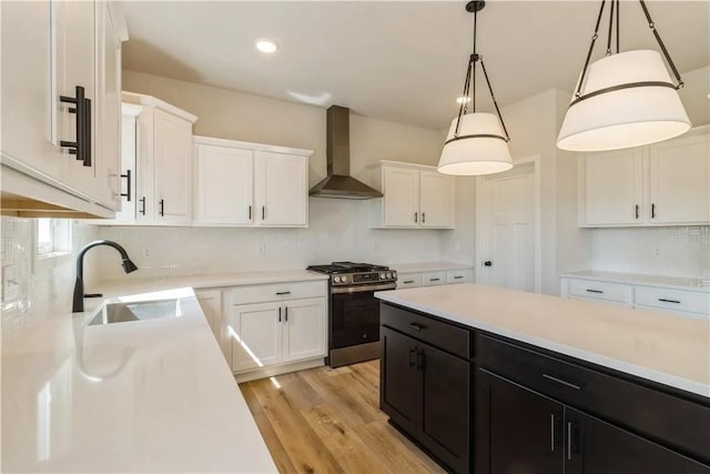 kitchen with stainless steel gas range, decorative light fixtures, wall chimney range hood, white cabinetry, and sink