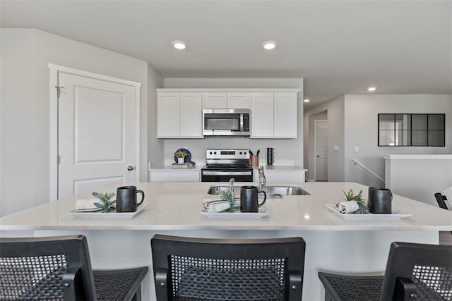 kitchen with a breakfast bar, a kitchen island with sink, white cabinets, sink, and stainless steel appliances