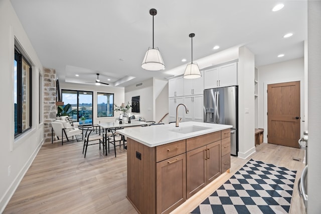 kitchen featuring pendant lighting, sink, stainless steel refrigerator with ice dispenser, an island with sink, and white cabinetry