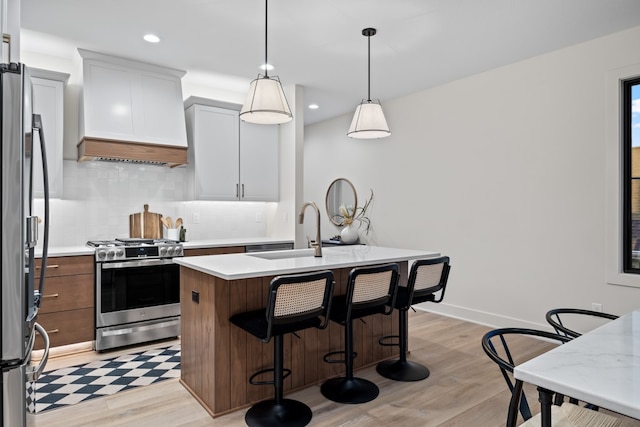 kitchen featuring white cabinetry, sink, a center island with sink, custom exhaust hood, and appliances with stainless steel finishes