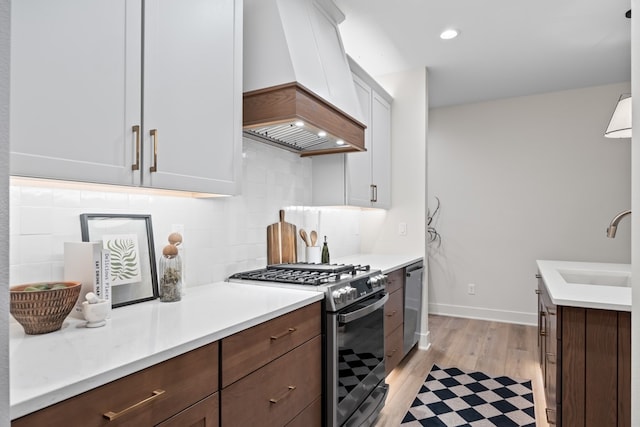 kitchen with sink, stainless steel appliances, light hardwood / wood-style flooring, premium range hood, and white cabinets