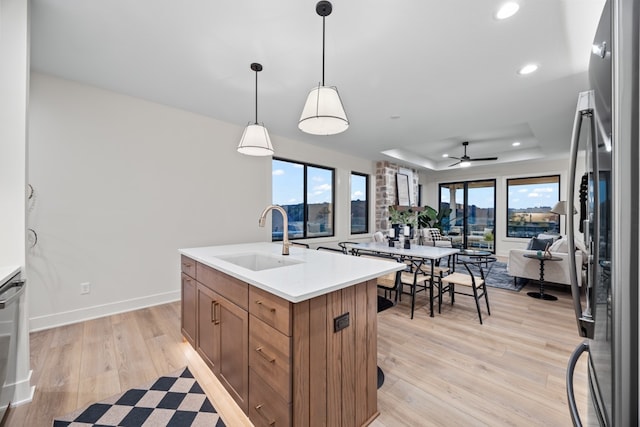 kitchen featuring ceiling fan, sink, a raised ceiling, stainless steel fridge, and a kitchen island with sink