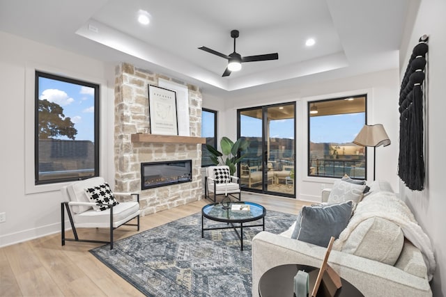 living room featuring a raised ceiling, a fireplace, light hardwood / wood-style floors, and plenty of natural light