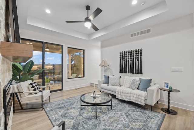 living room with ceiling fan, a raised ceiling, and light wood-type flooring