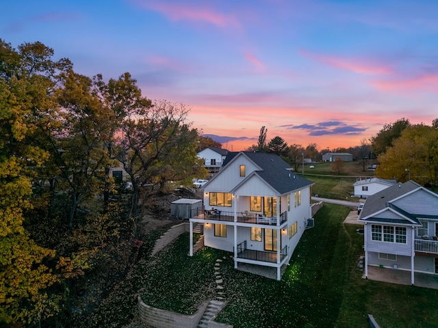 back house at dusk featuring a yard and a balcony