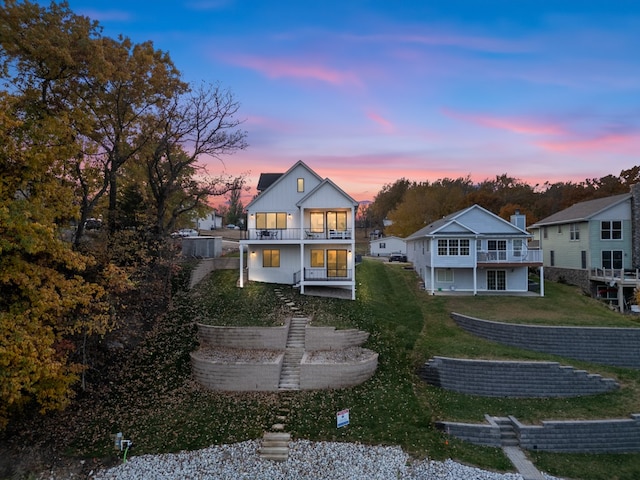 back house at dusk with a patio area, a balcony, and a yard