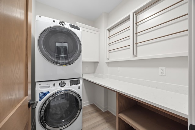 clothes washing area with cabinets, light wood-type flooring, and stacked washer and clothes dryer