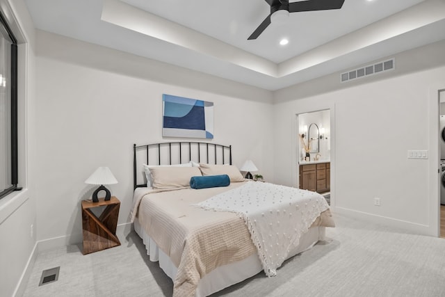 bedroom featuring connected bathroom, a tray ceiling, ceiling fan, and stacked washer and clothes dryer