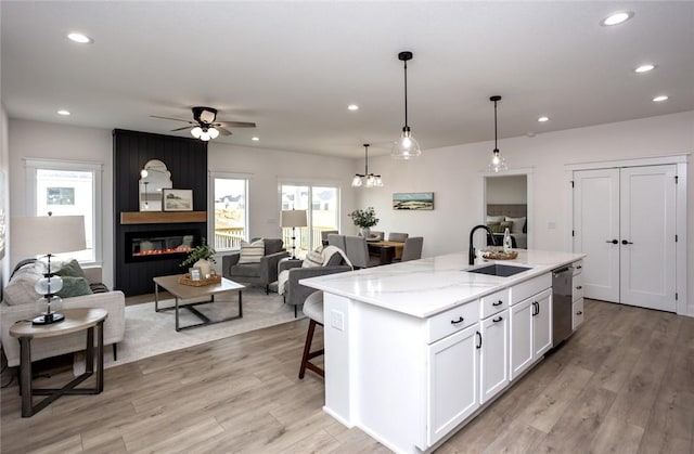 kitchen with white cabinetry, a large fireplace, sink, stainless steel dishwasher, and a center island with sink