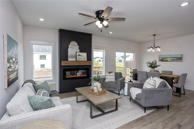 living room featuring a fireplace, ceiling fan with notable chandelier, and light hardwood / wood-style flooring