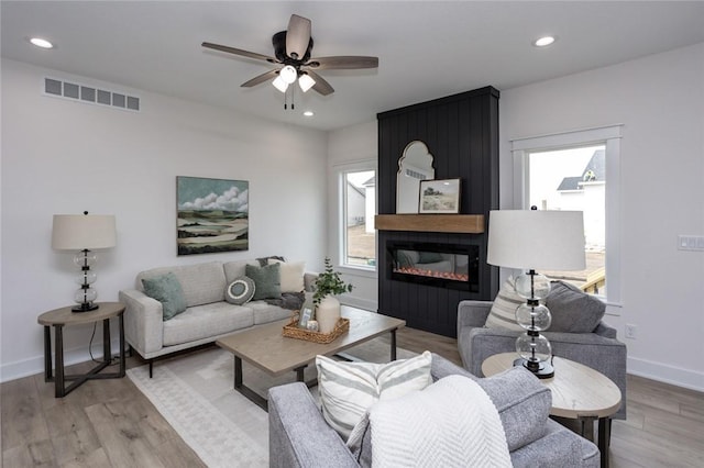 living room with light wood-type flooring, a large fireplace, and ceiling fan