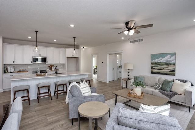 living room with ceiling fan, light wood-type flooring, and sink