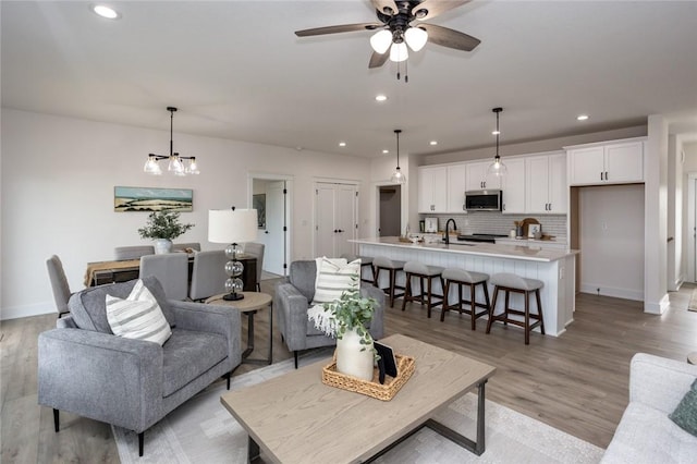 living room featuring ceiling fan with notable chandelier, light hardwood / wood-style floors, and sink