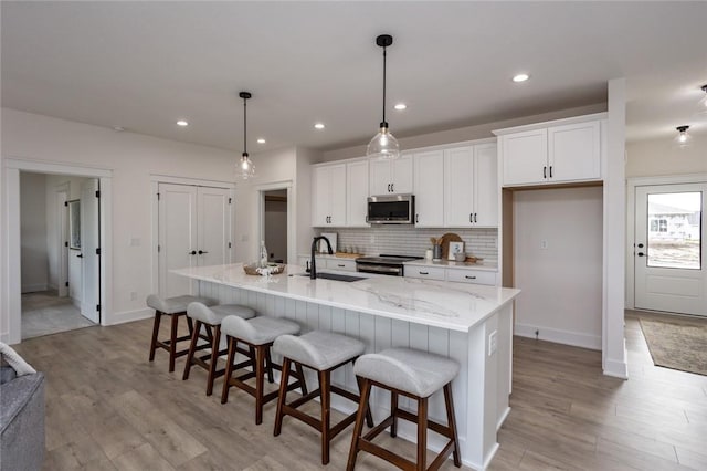 kitchen featuring a center island with sink, white cabinets, sink, appliances with stainless steel finishes, and decorative light fixtures