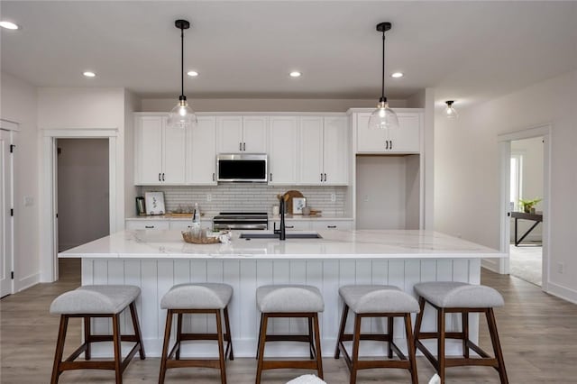 kitchen featuring a large island with sink, stainless steel appliances, light stone counters, and sink