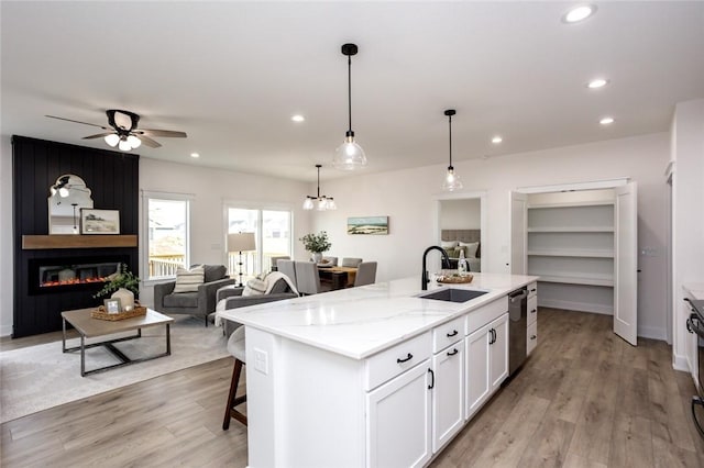 kitchen with ceiling fan with notable chandelier, a large fireplace, sink, a center island with sink, and white cabinetry