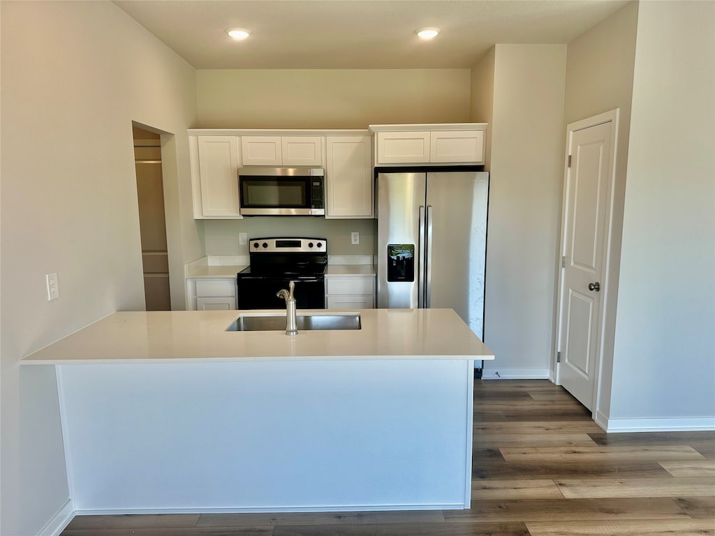 kitchen with an island with sink, light wood-type flooring, white cabinets, sink, and appliances with stainless steel finishes