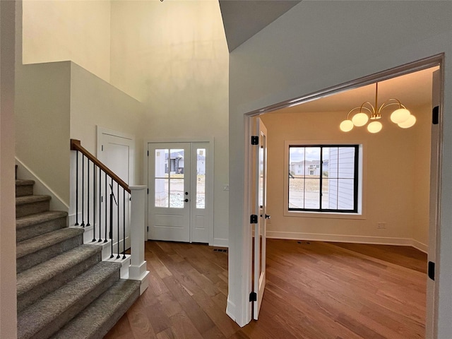 entrance foyer featuring a healthy amount of sunlight, wood-type flooring, a towering ceiling, and a chandelier