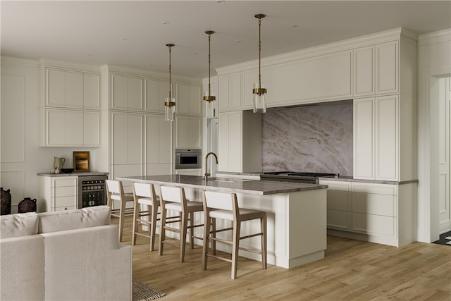 kitchen with decorative backsplash, an island with sink, sink, oven, and light hardwood / wood-style floors