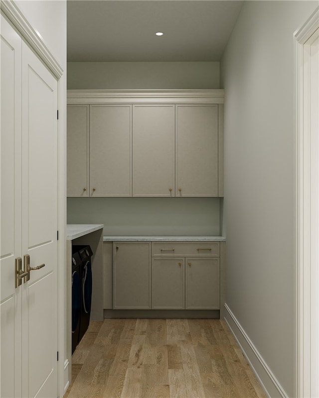 clothes washing area with cabinets, washing machine and dryer, and light wood-type flooring