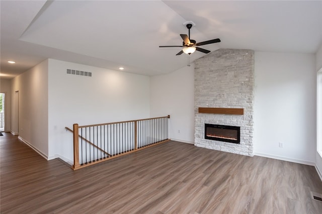 unfurnished living room featuring hardwood / wood-style flooring, vaulted ceiling, ceiling fan, and a stone fireplace