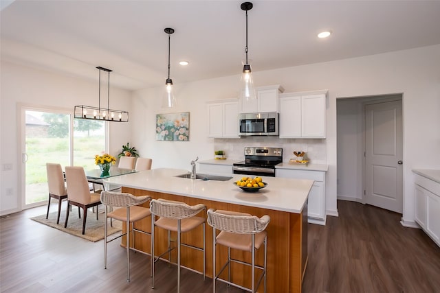 kitchen with white cabinets, dark hardwood / wood-style floors, stainless steel appliances, and a kitchen island with sink