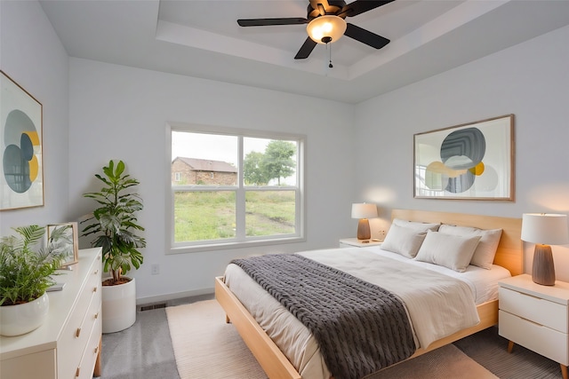 carpeted bedroom with ceiling fan and a tray ceiling