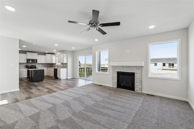 unfurnished living room featuring a stone fireplace, ceiling fan, and light hardwood / wood-style flooring