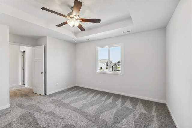 spare room with a tray ceiling, ceiling fan, and light colored carpet