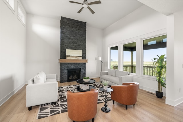 living room with a stone fireplace, light hardwood / wood-style flooring, and ceiling fan