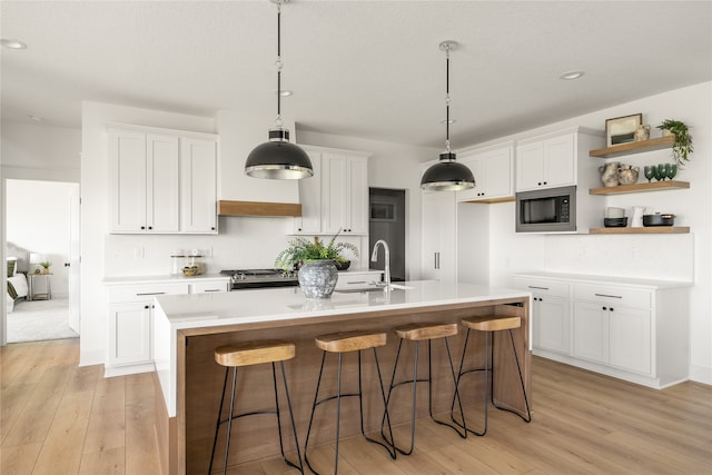 kitchen featuring built in microwave, white cabinetry, a kitchen island with sink, and a breakfast bar