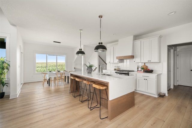 kitchen featuring custom exhaust hood, stainless steel stove, a kitchen island with sink, and white cabinets