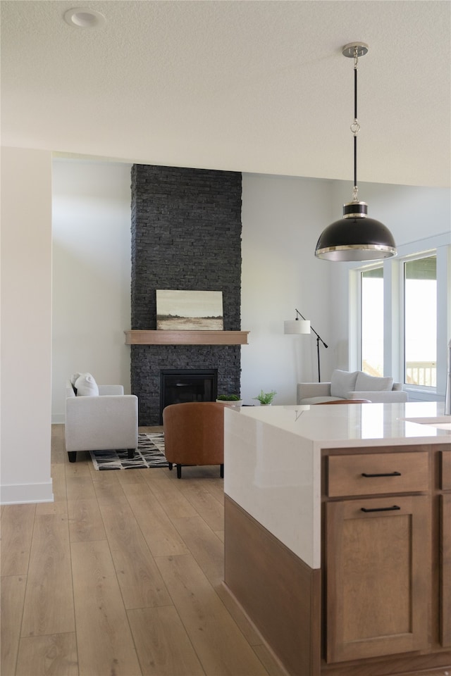 kitchen with a stone fireplace, a textured ceiling, light hardwood / wood-style floors, and decorative light fixtures