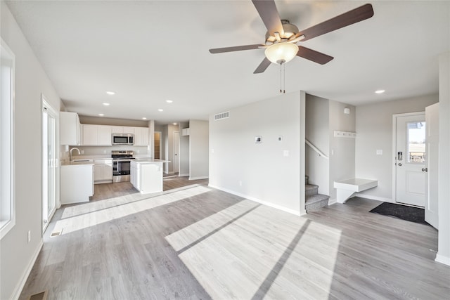 unfurnished living room featuring ceiling fan, light wood-type flooring, and sink