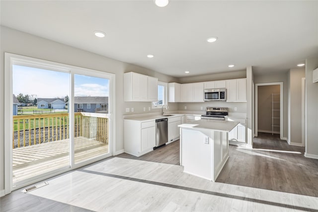 kitchen featuring white cabinetry, sink, appliances with stainless steel finishes, a kitchen island, and light wood-type flooring